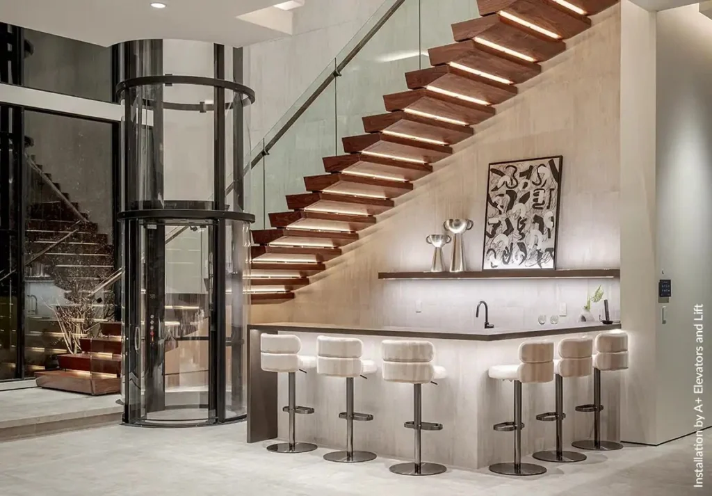 Round Savaria Vuelift acrylic home elevator installed beside a modern staircase in a luxury Florida residence