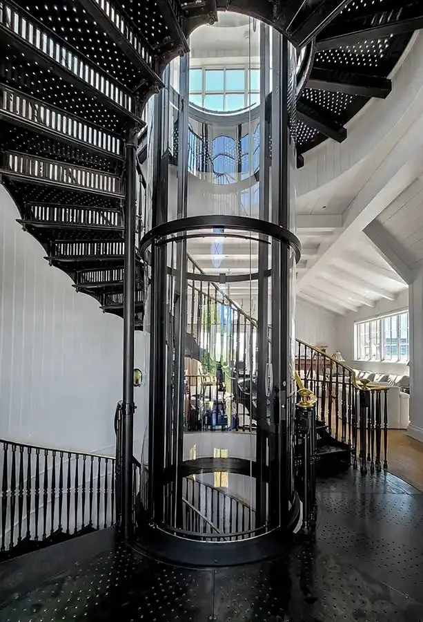 Savaria Vuelift round acrylic residential elevator installed between black metal staircases in a luxury Florida home